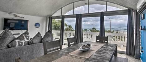 A dining area with a table and chairs, a sofa with cushions, and a TV on the wall.