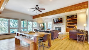 A spacious living area with a wooden dining table, a sofa, and a fireplace. - Modern Fischer House w/ Deck, Fire Pit & Hot Tub! (Canyon Lake)