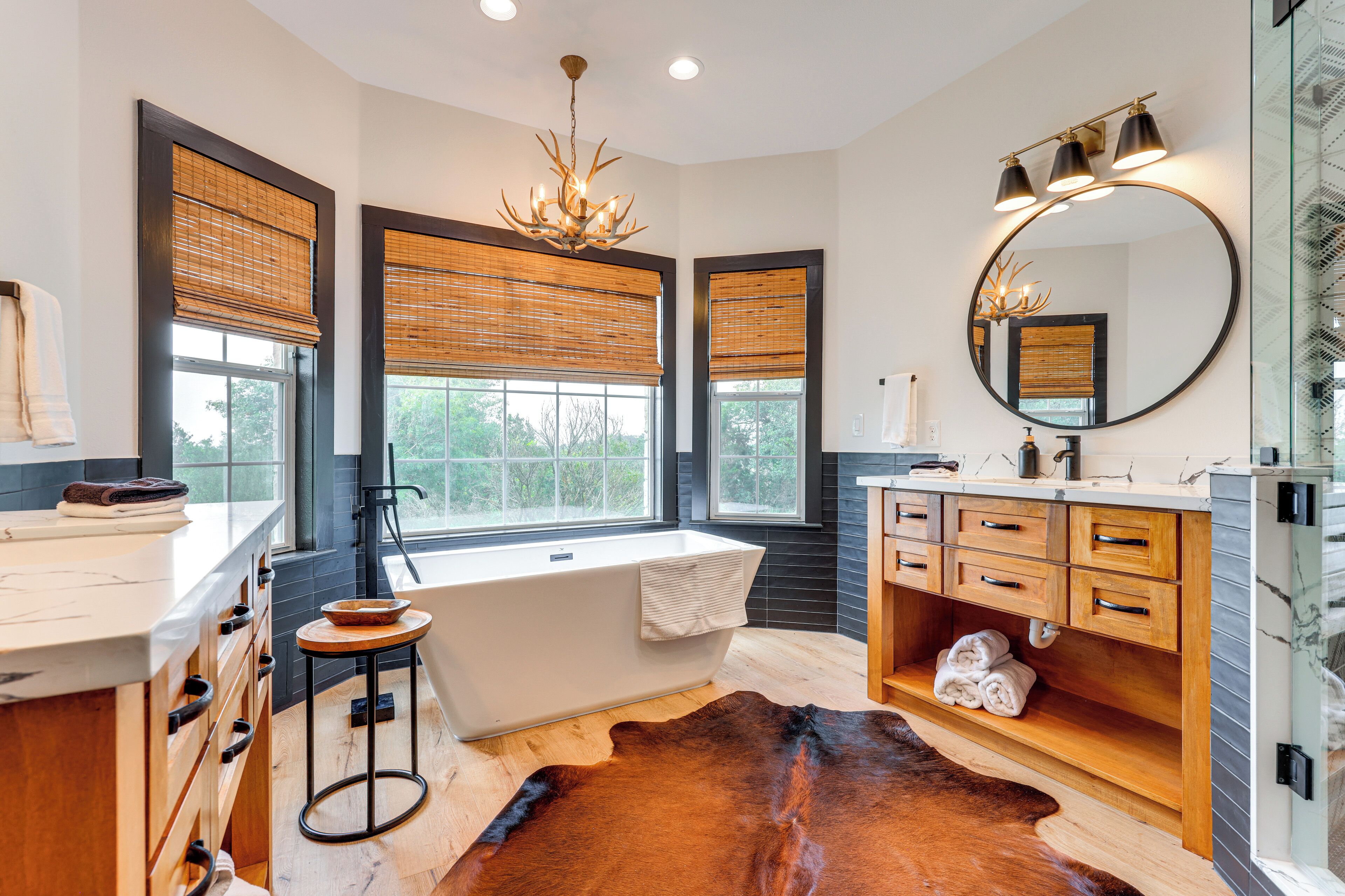 A modern bathroom with a bathtub, vanity, and large windows with blinds.