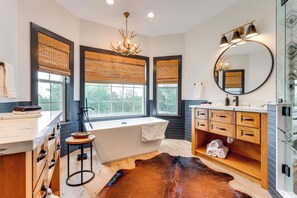 A modern bathroom with a bathtub, vanity, and large windows with blinds.