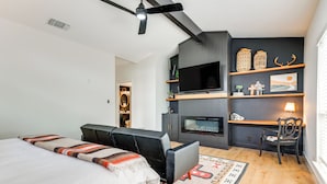 A modern bedroom with a bed, a sofa, a TV, a fireplace, and a desk area. - Modern Fischer House w/ Deck, Fire Pit & Hot Tub! (Canyon Lake)