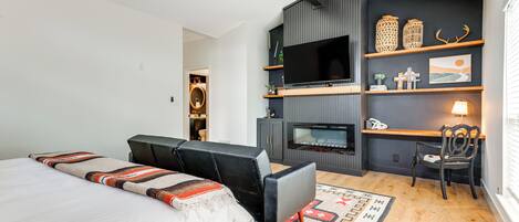 Un dormitorio moderno con cama, sofá, televisión, chimenea y zona de escritorio.