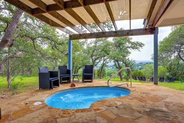 A stone pool with a wooden deck and chairs, surrounded by trees.