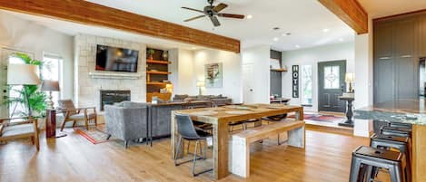 Amplia sala de estar con una gran mesa de comedor de madera, asientos cómodos, una chimenea y una cocina con taburetes de bar.