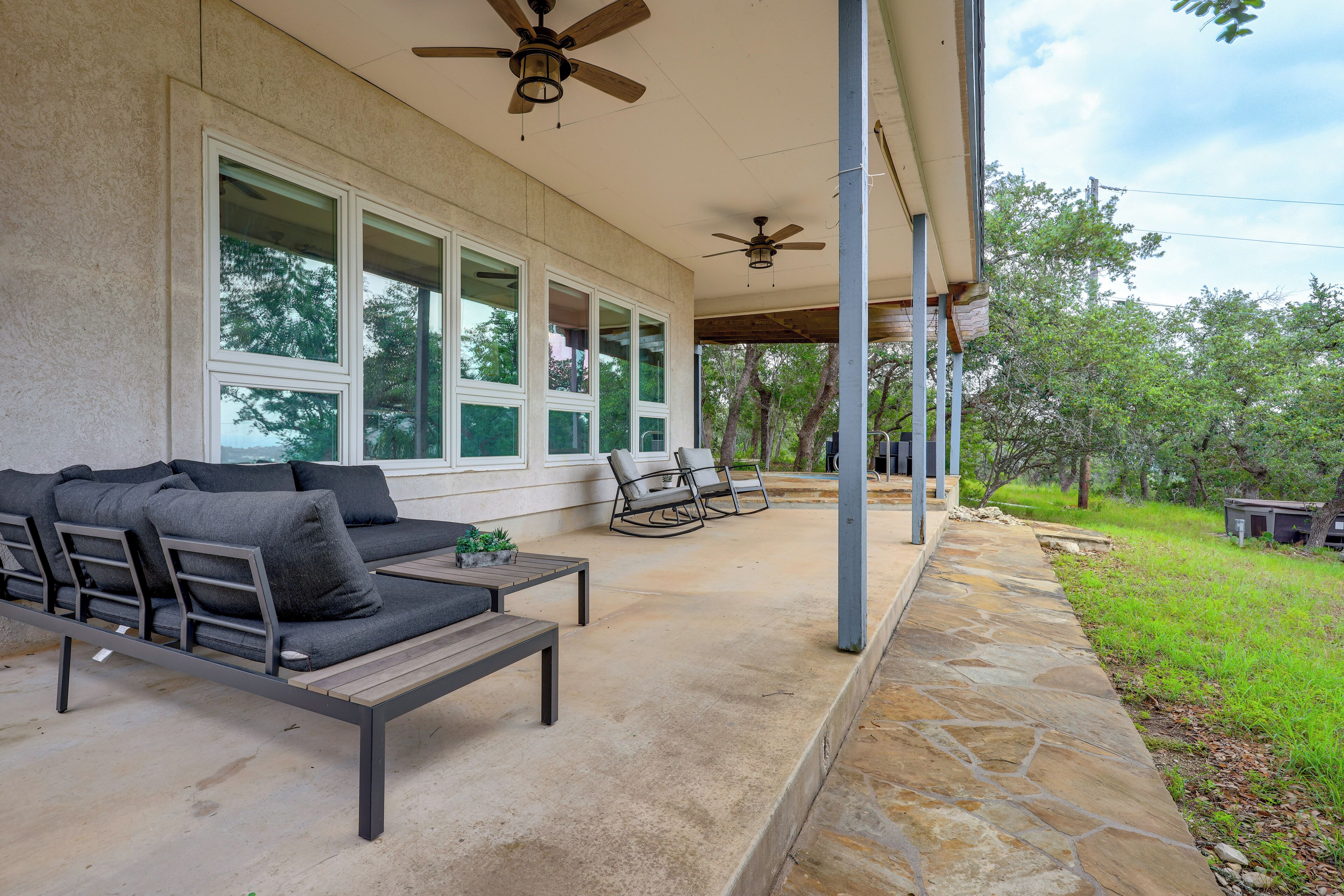 A covered patio area with a sofa and chairs, large windows, and ceiling fans.