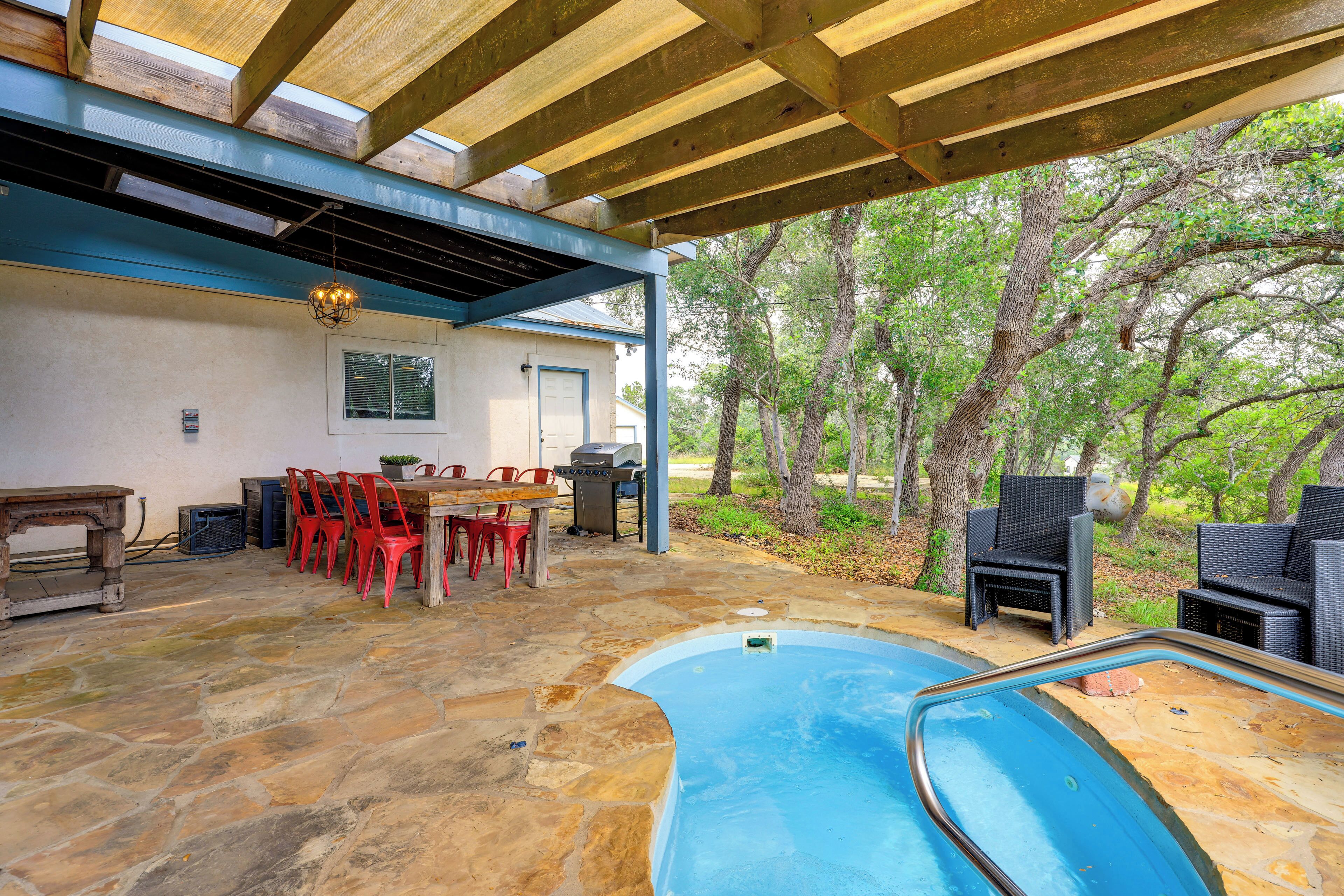 A stone patio with a pool, outdoor furniture, and a covered seating area.