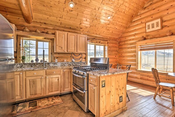 A log cabin kitchen with wooden cabinets, a granite countertop, stainless steel appliances, and large windows offering views of the outdoors. - 22str-00360 Fairplay Cabin w/ Fire Pit, Mtn Views! (Como)