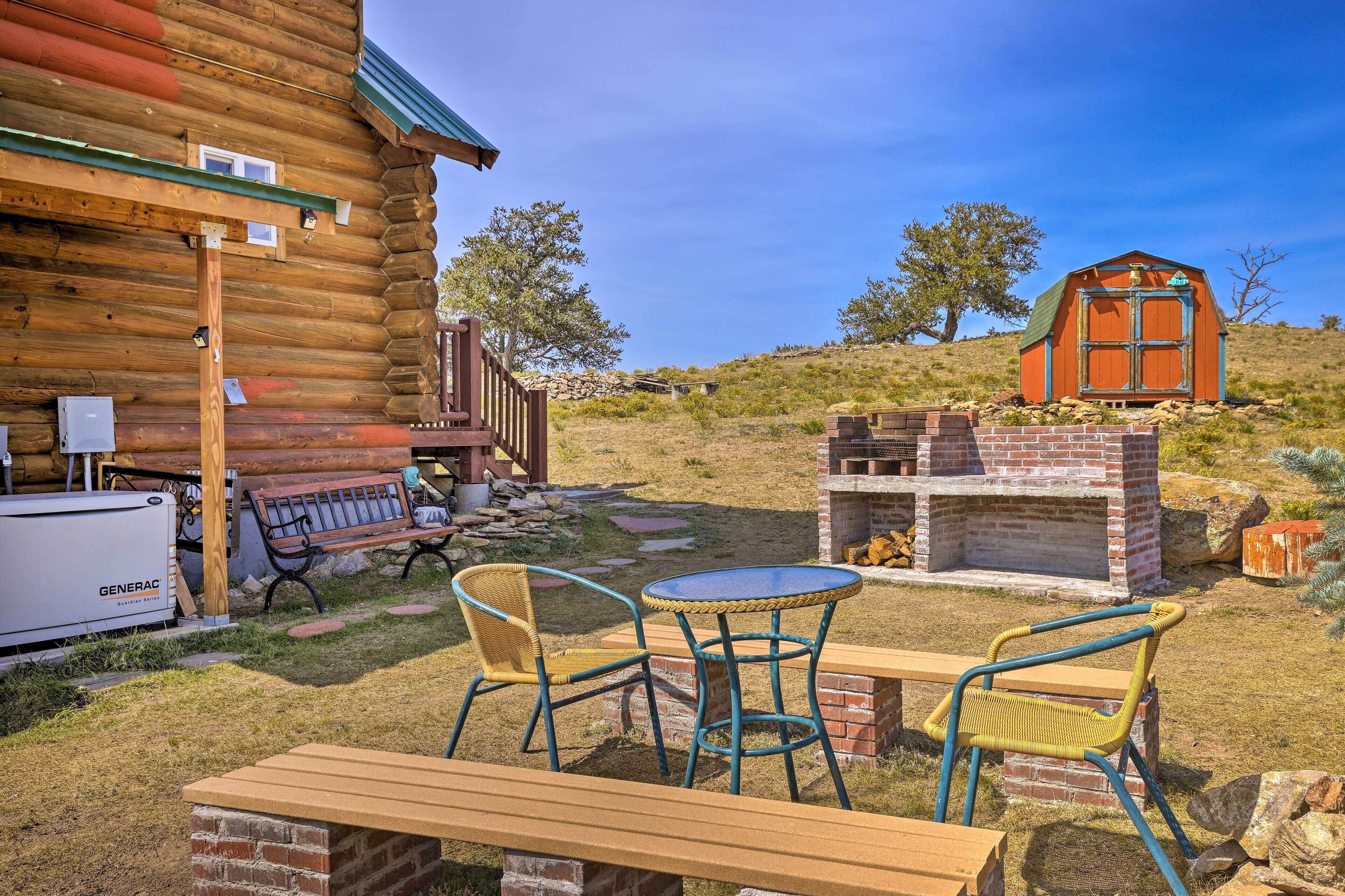 Une cabane en rondins dotée d’un patio comprenant une table et des chaises, un barbecue et un petit abri de jardin.