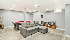 Uma sala de estar moderna com um sofá modular cinza, mesa de bilhar e alvo de dardos.