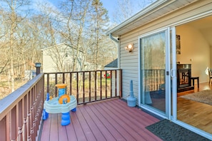 A wooden deck with a water fountain, a sliding glass door leading to a room, and a view of trees and a red vehicle in the background.