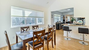 Cozinha moderna com ilha central, mesa de jantar de madeira com cadeiras e um espaço bar com banquetas.
