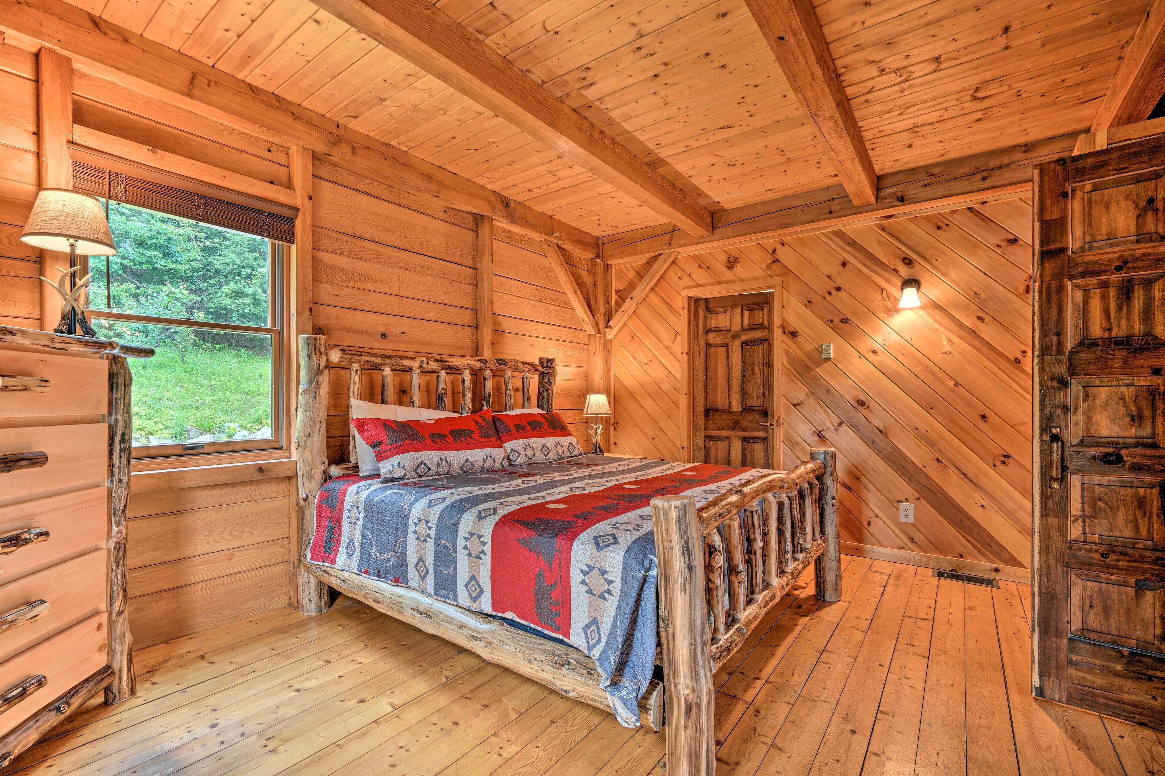 A wooden cabin bedroom with a bed, dresser, window, and a door.