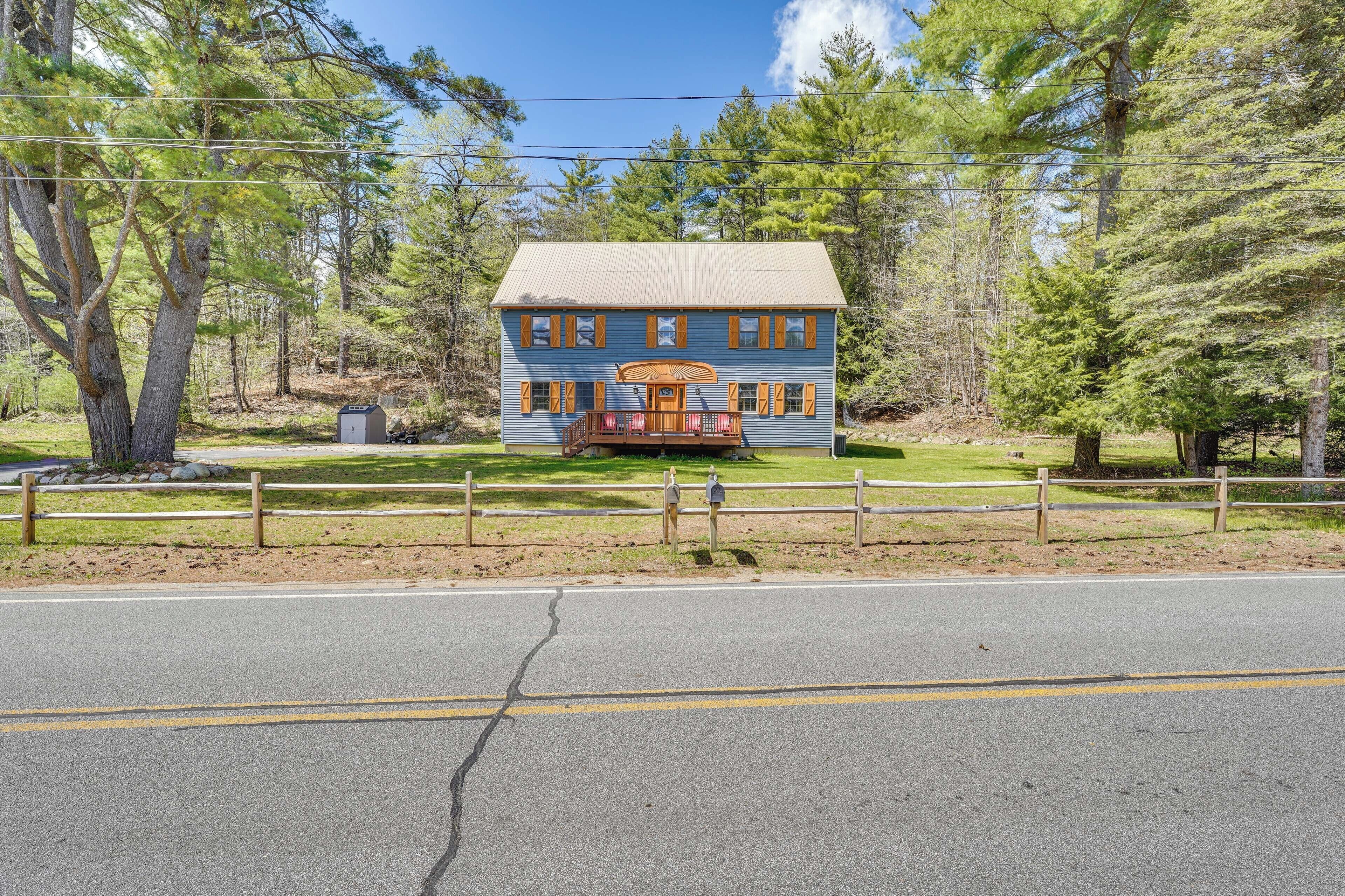 A two-story house with a porch, surrounded by trees and a wooden fence.