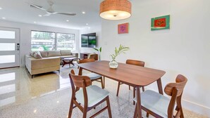 A modern dining area with a wooden table and chairs, a hanging light fixture, and a view of the outdoors through large windows. - Charming Sarasota Vacation Home Near Downtown (Sarasota)