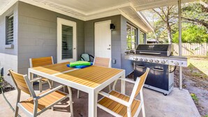 A covered patio with a wooden table and chairs, a grill, and a door leading to a garage. - Charming Sarasota Vacation Home Near Downtown (Sarasota)