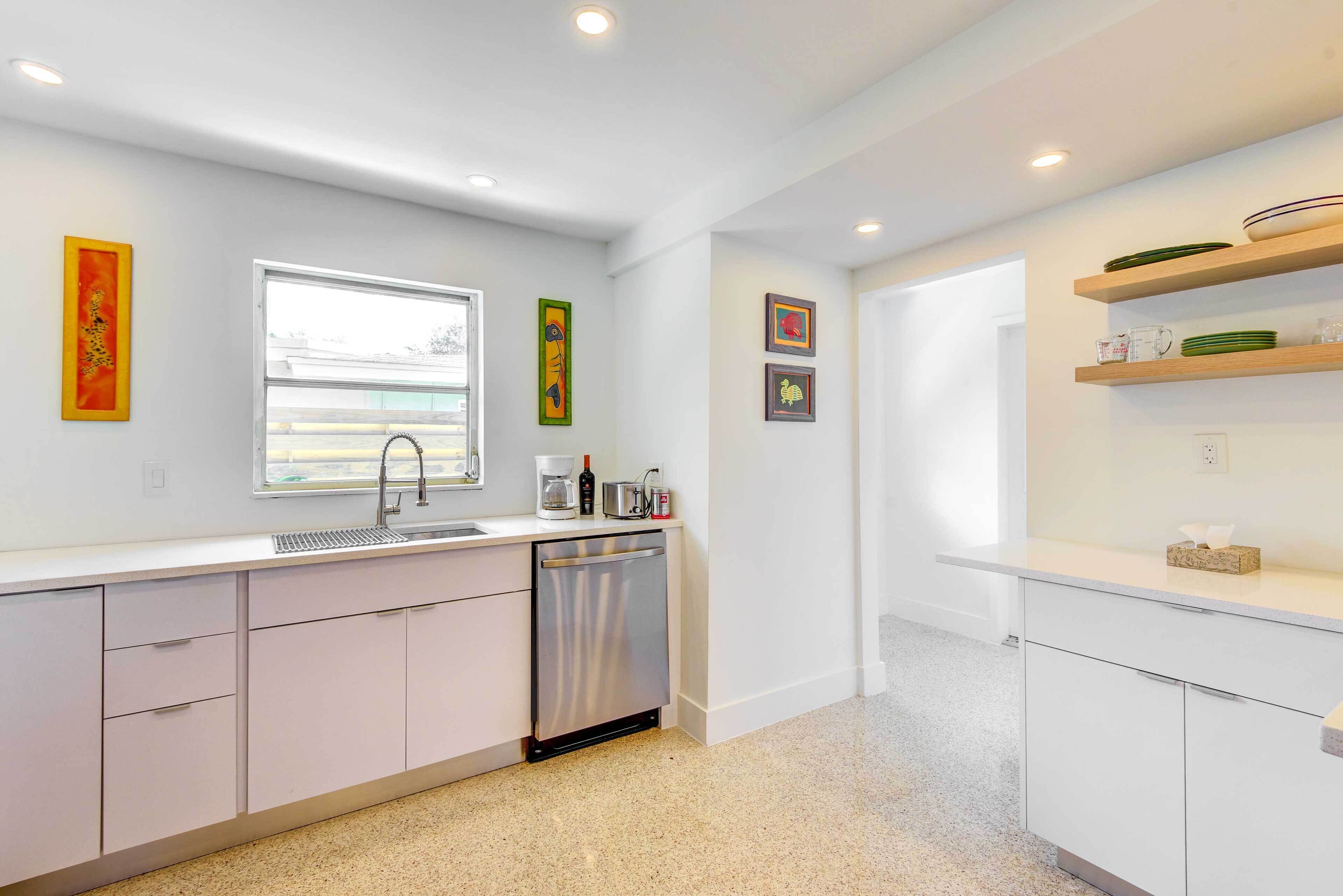 A modern kitchen with white cabinets, a stainless steel dishwasher, and a window providing natural light.