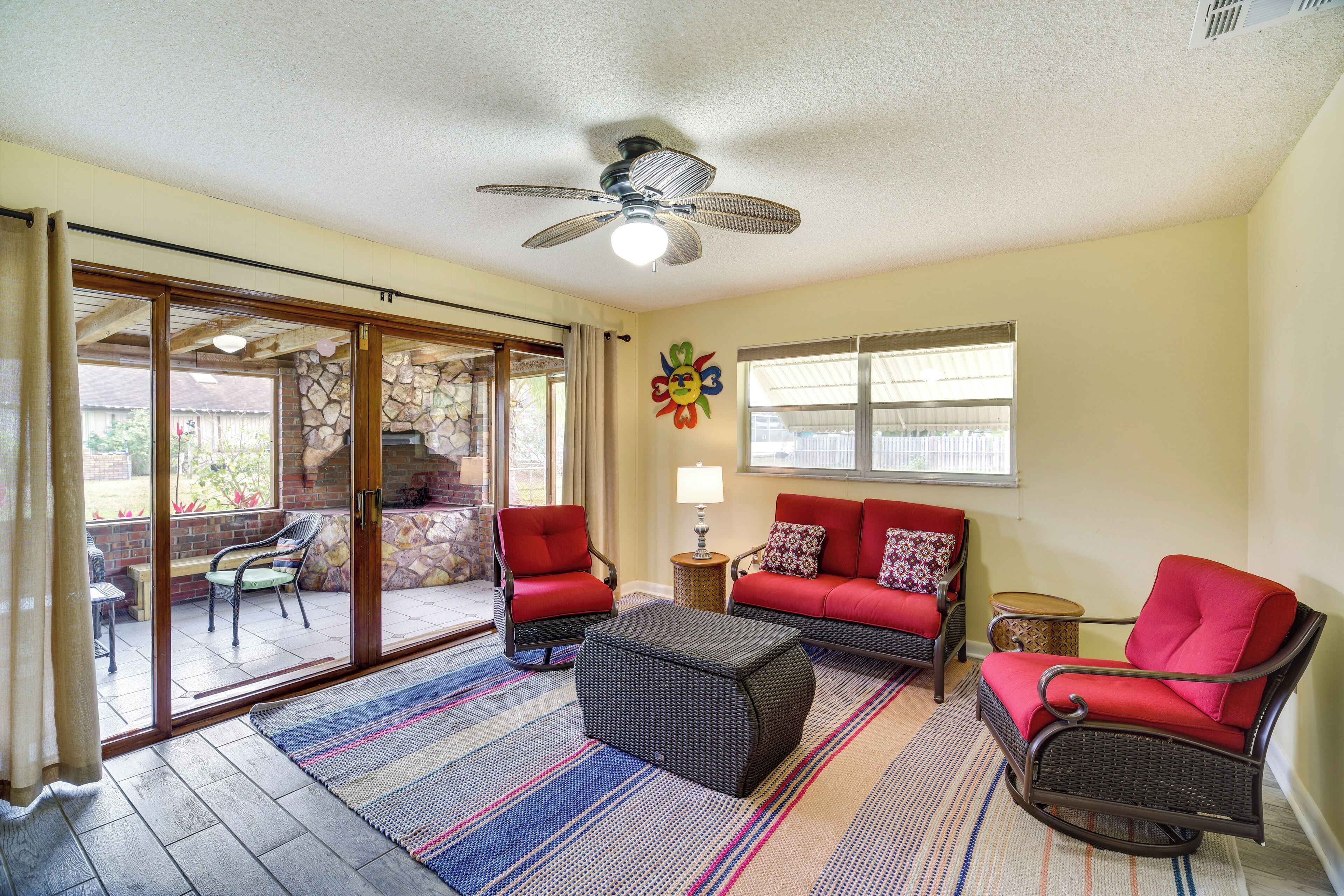 A spacious living area with a sliding glass door leading to a patio, a ceiling fan, and a red sofa set.