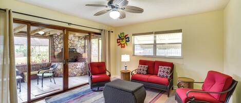 A spacious living area with a sliding glass door leading to a patio, a ceiling fan, and a red sofa set.