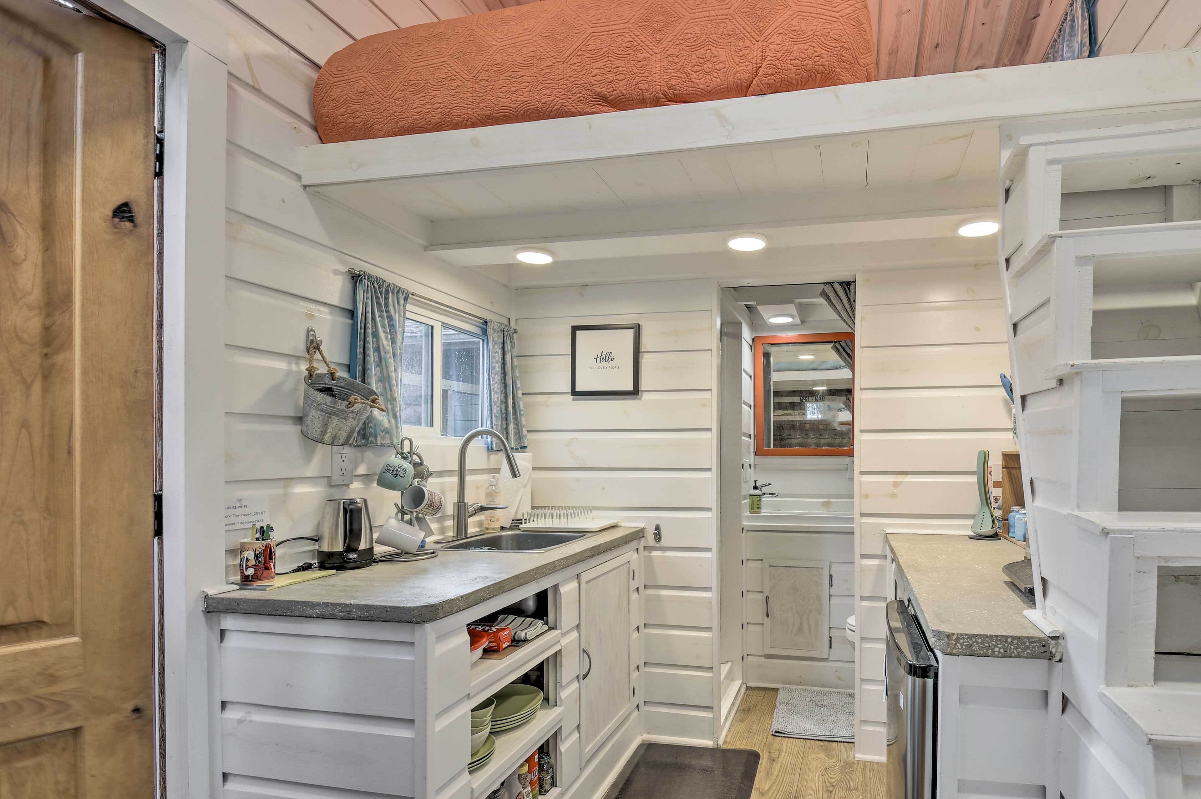 A compact kitchen with white cabinetry, a built-in oven, a sink, and a window with curtains.