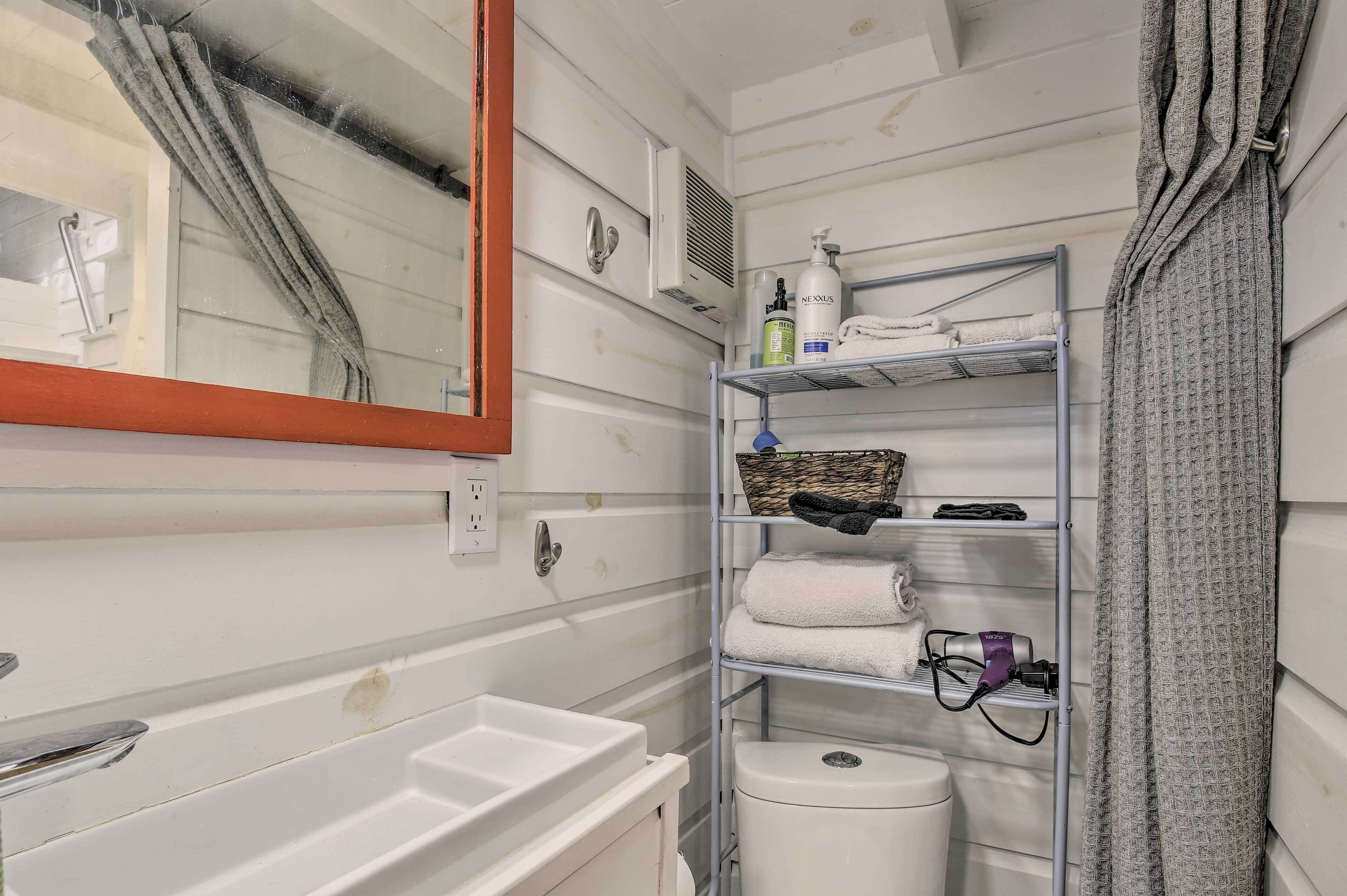 A bathroom with a white sink, a mirror, a shelf with towels and toiletries, and a shower curtain.