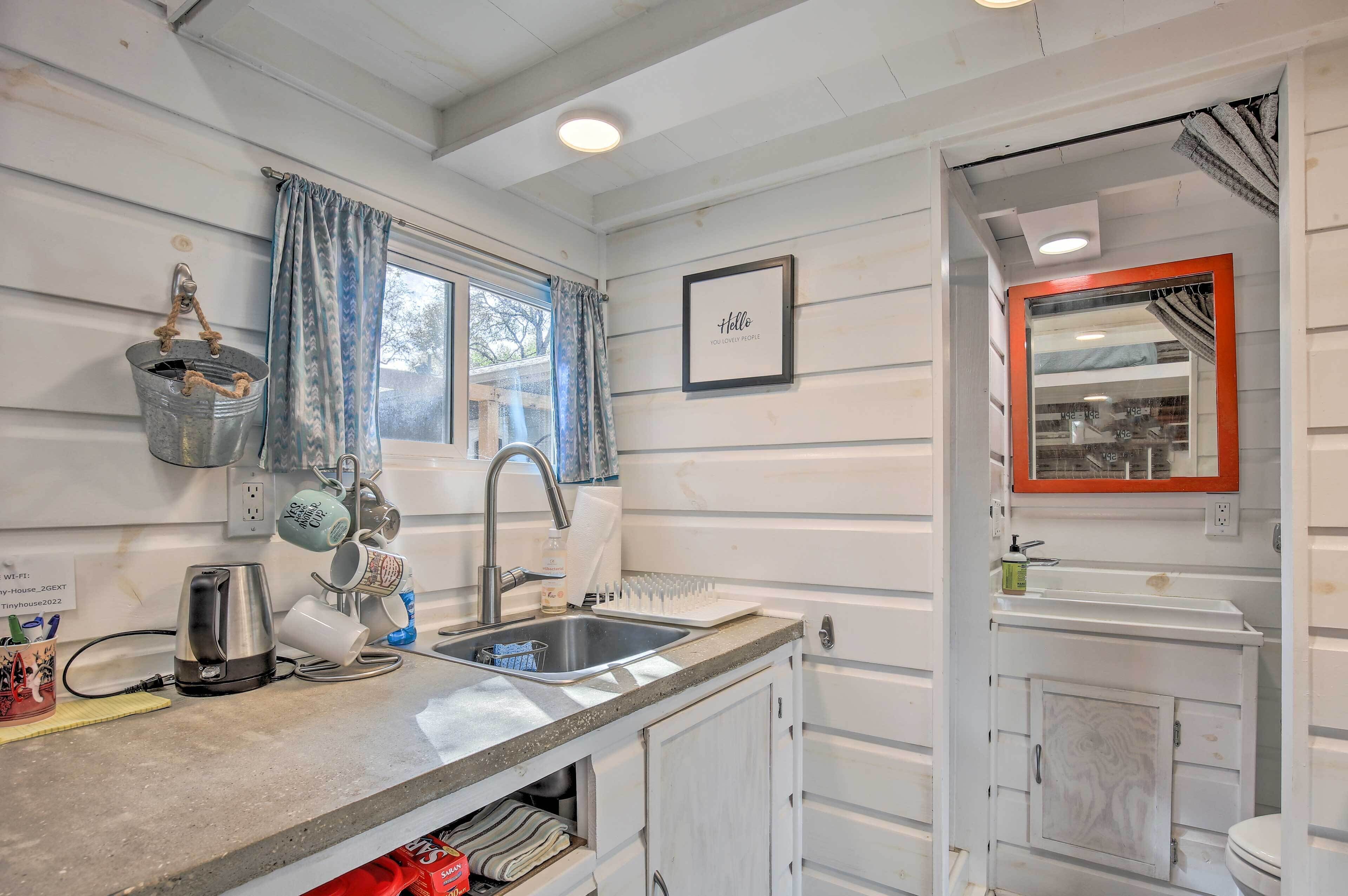 A compact kitchen with a sink, kettle, and a window with curtains.