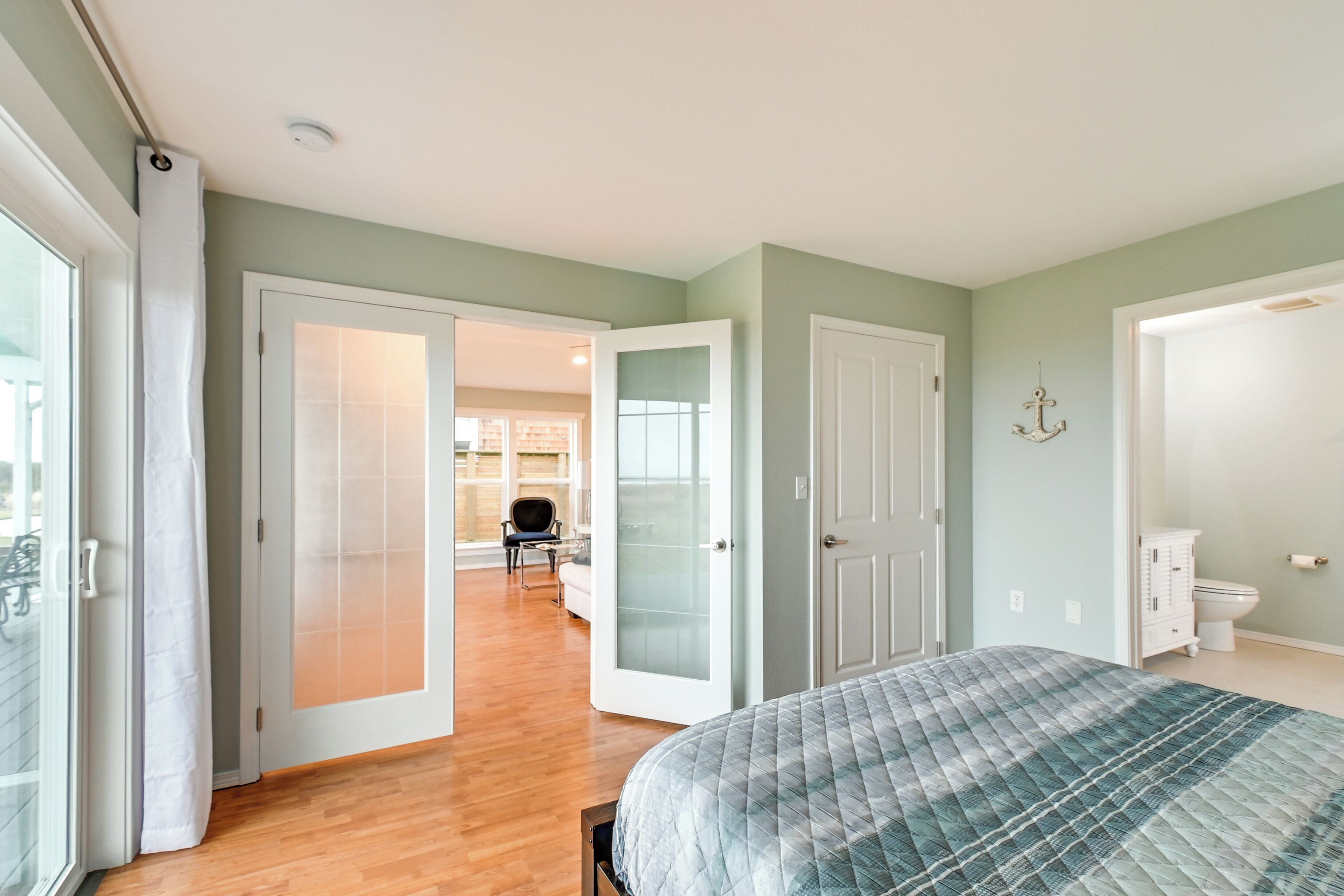 A bedroom with a bed, a door leading to another room, and a view of a living area.