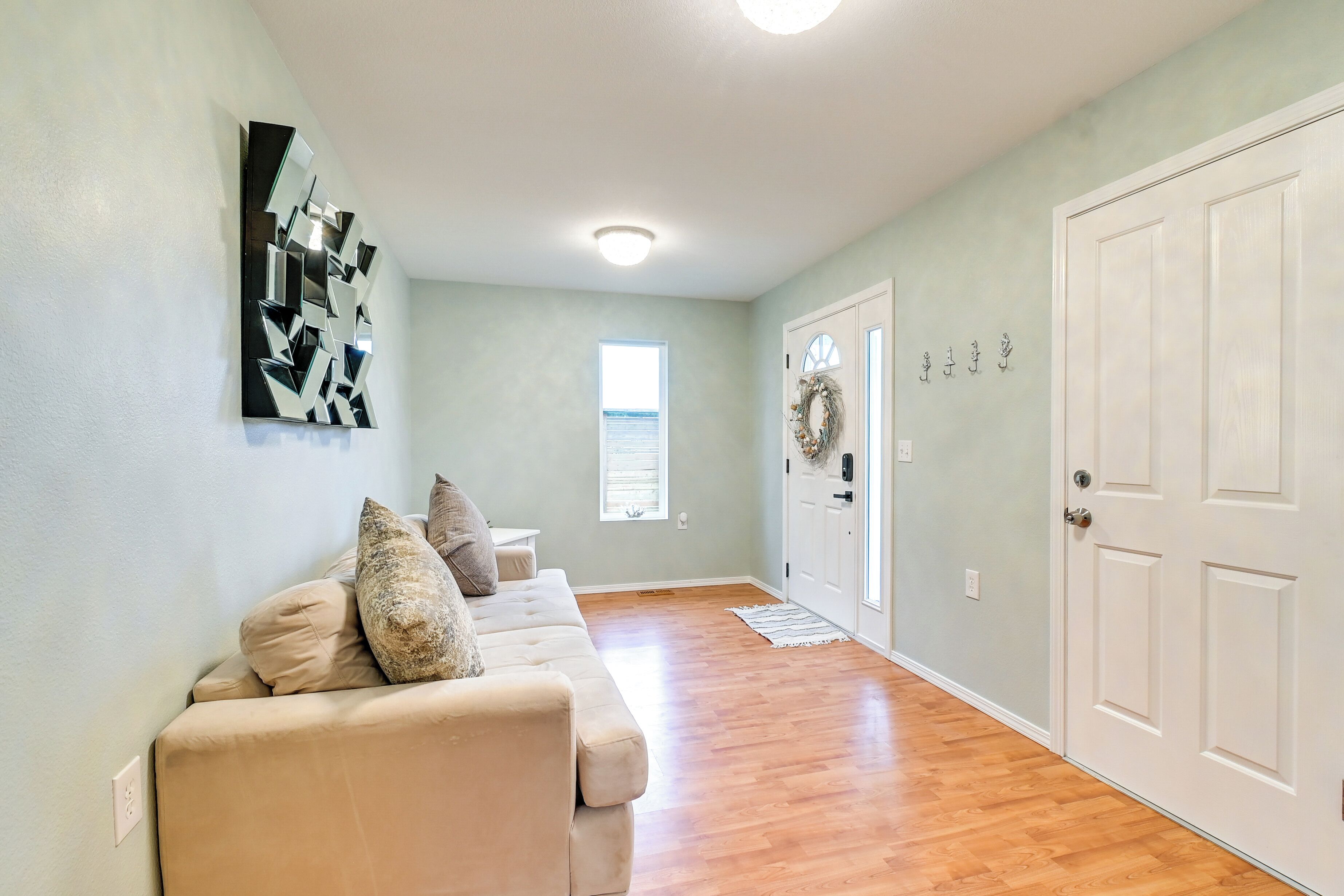 A hallway with a beige couch, a wall-mounted abstract art piece, a door with a wreath, and a window with blinds.