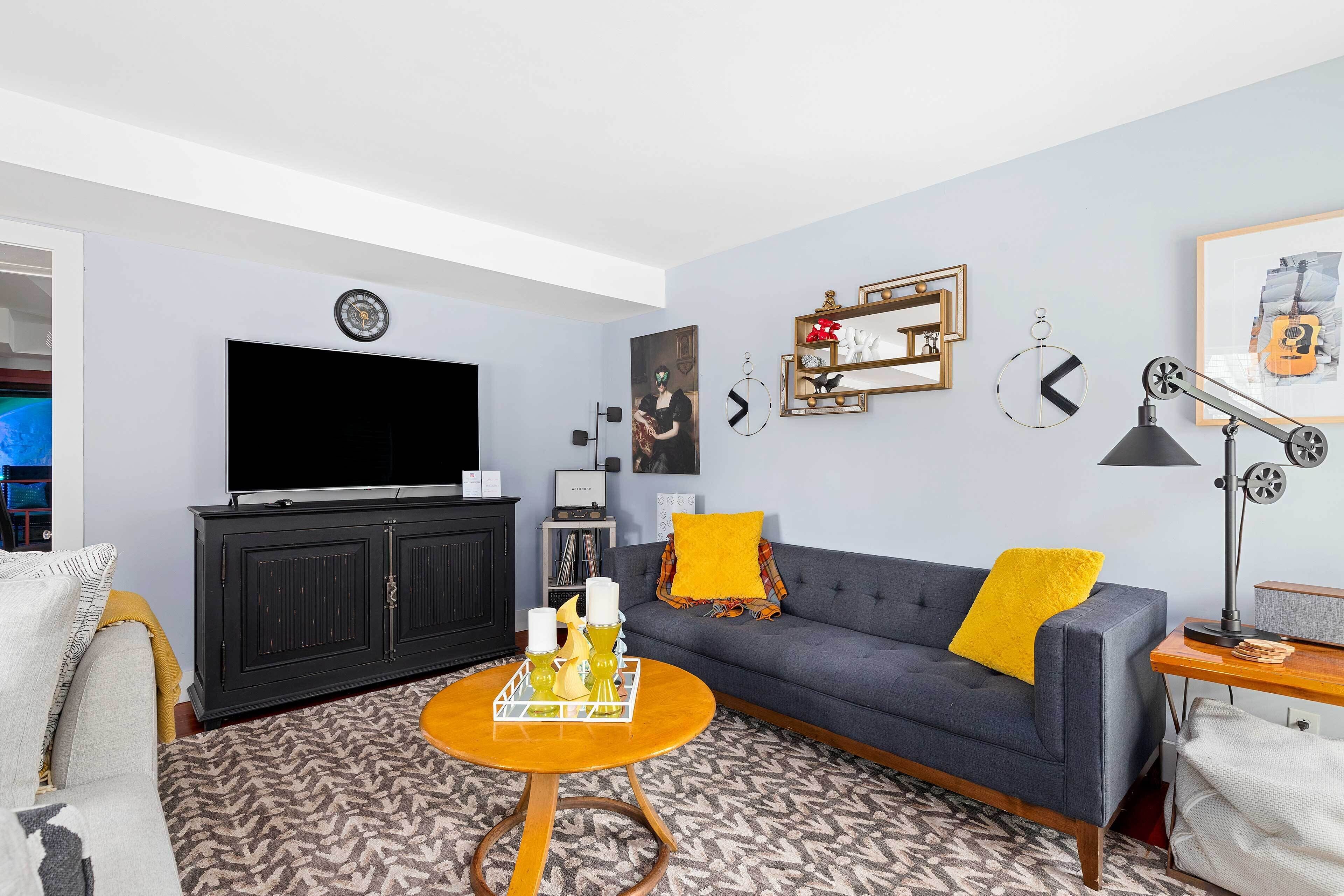 Ein Wohnzimmer mit grauem Sofa, einem Holztisch, einer schwarzen Unterhaltungsanlage und einem Flachbildfernseher.