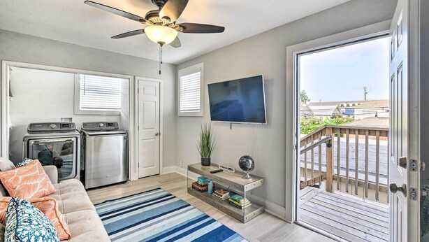 A modern living room with a sofa, a coffee table, a TV, a ceiling fan, a kitchen with appliances, and a balcony with a railing. - ~ 1 Mi to Pier & Beaches! Family Home in Galveston (Galveston)