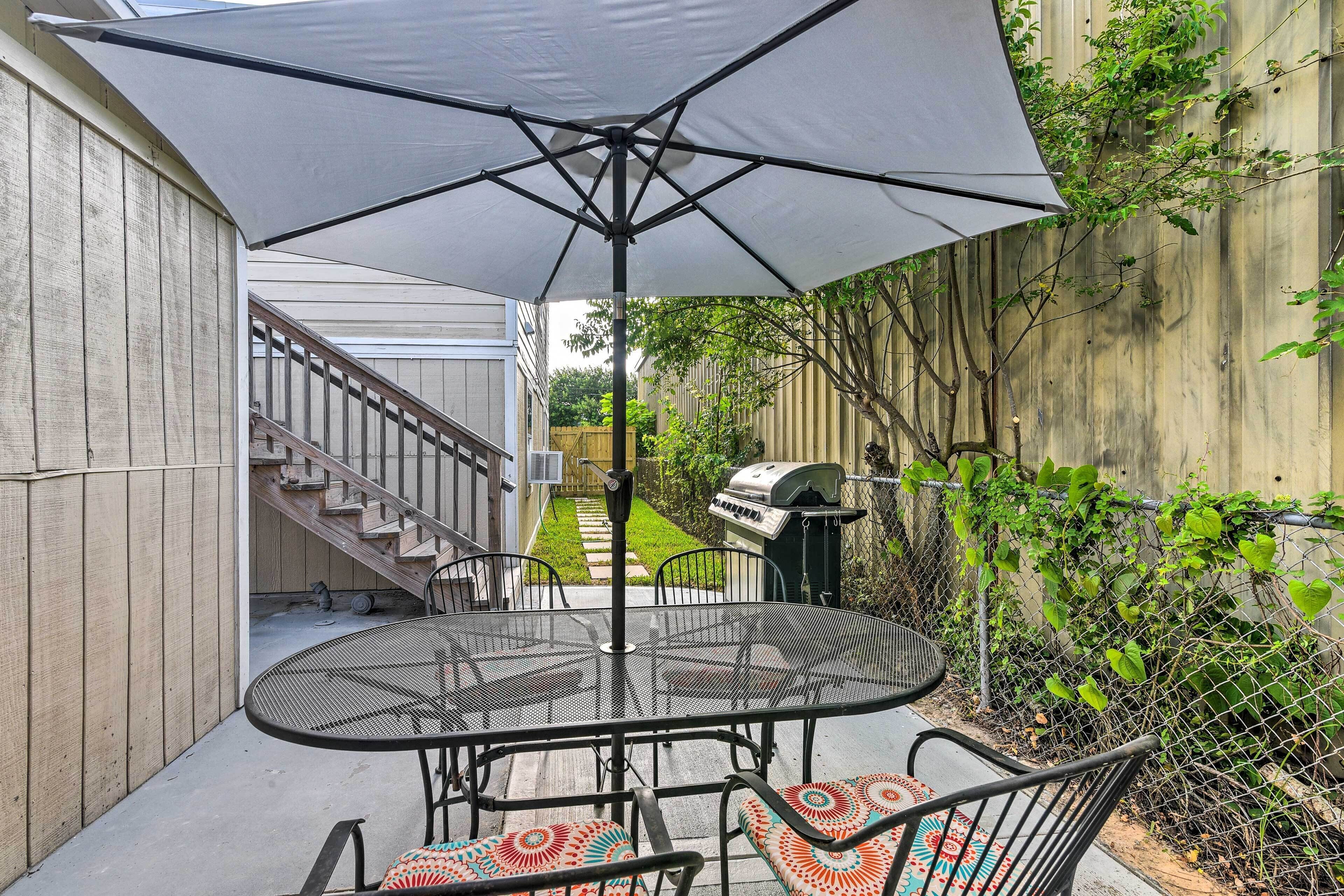 A patio with a round metal table and chairs, an umbrella, and a grill.
