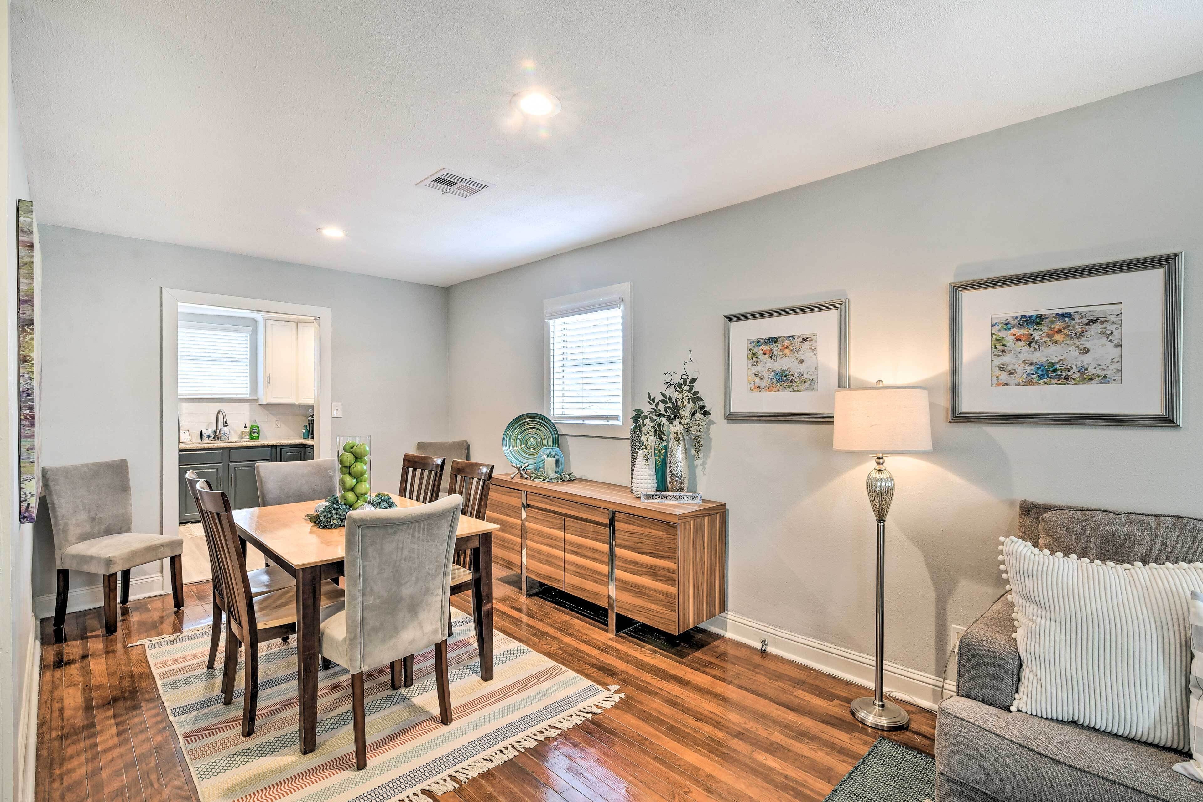 A dining area with a wooden table, chairs, and a buffet cabinet. There is a floor lamp and a couch in the background.