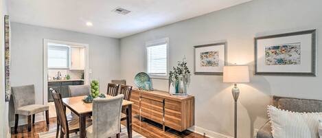 A dining area with a wooden table, chairs, and a buffet cabinet. There is a floor lamp and a couch in the background.