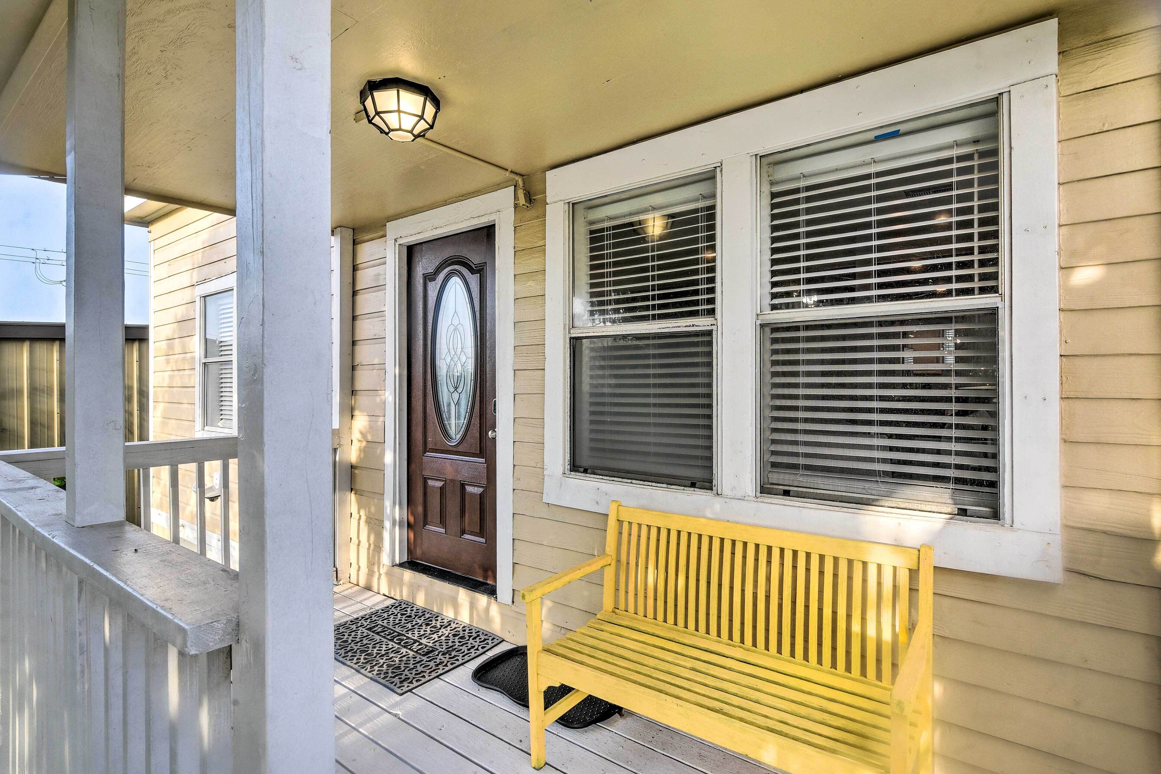 A porch with a bench, a door, and two windows with blinds.