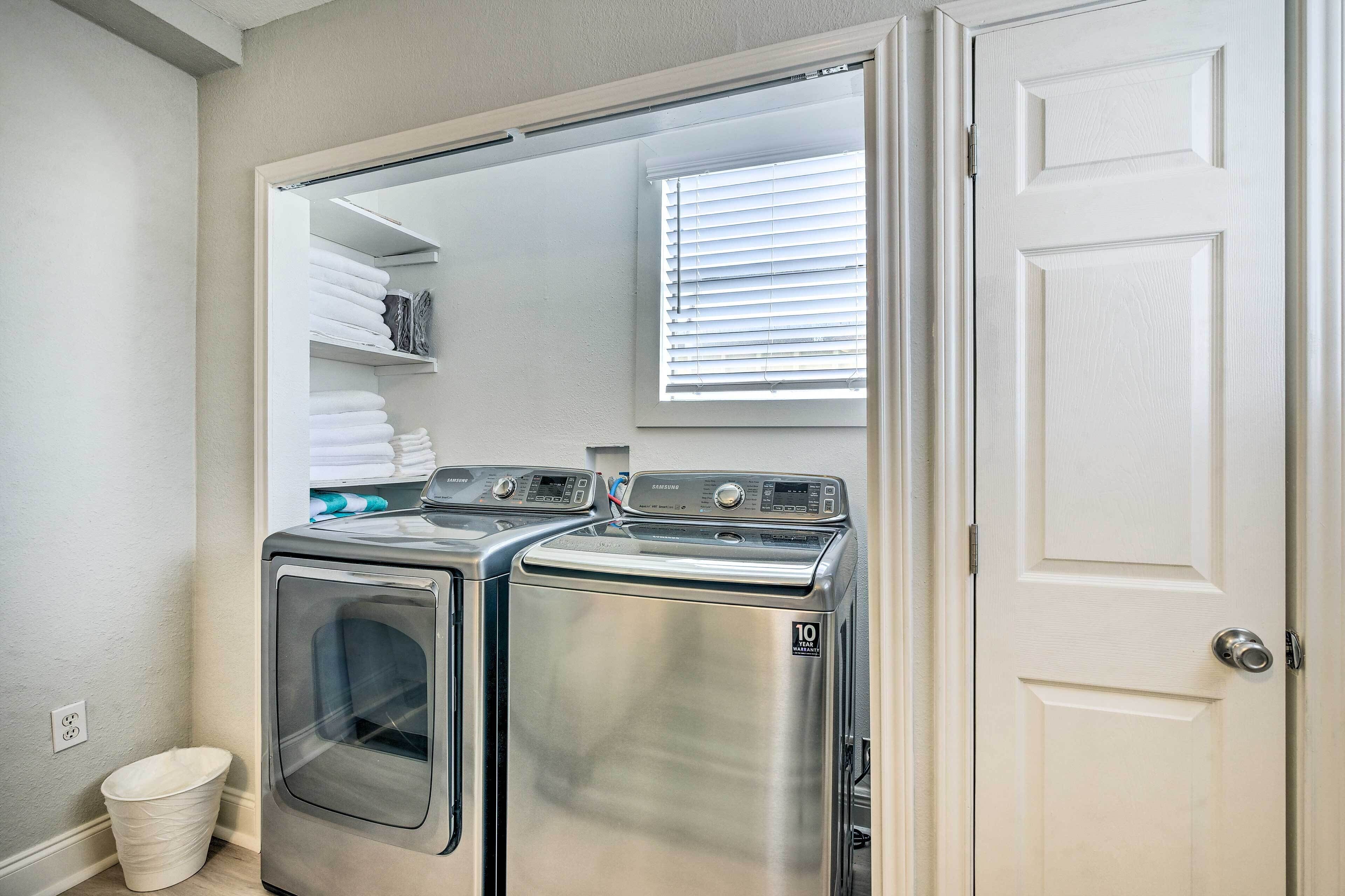 A laundry room with two stainless steel washers and dryers, a white door, and a window with blinds.