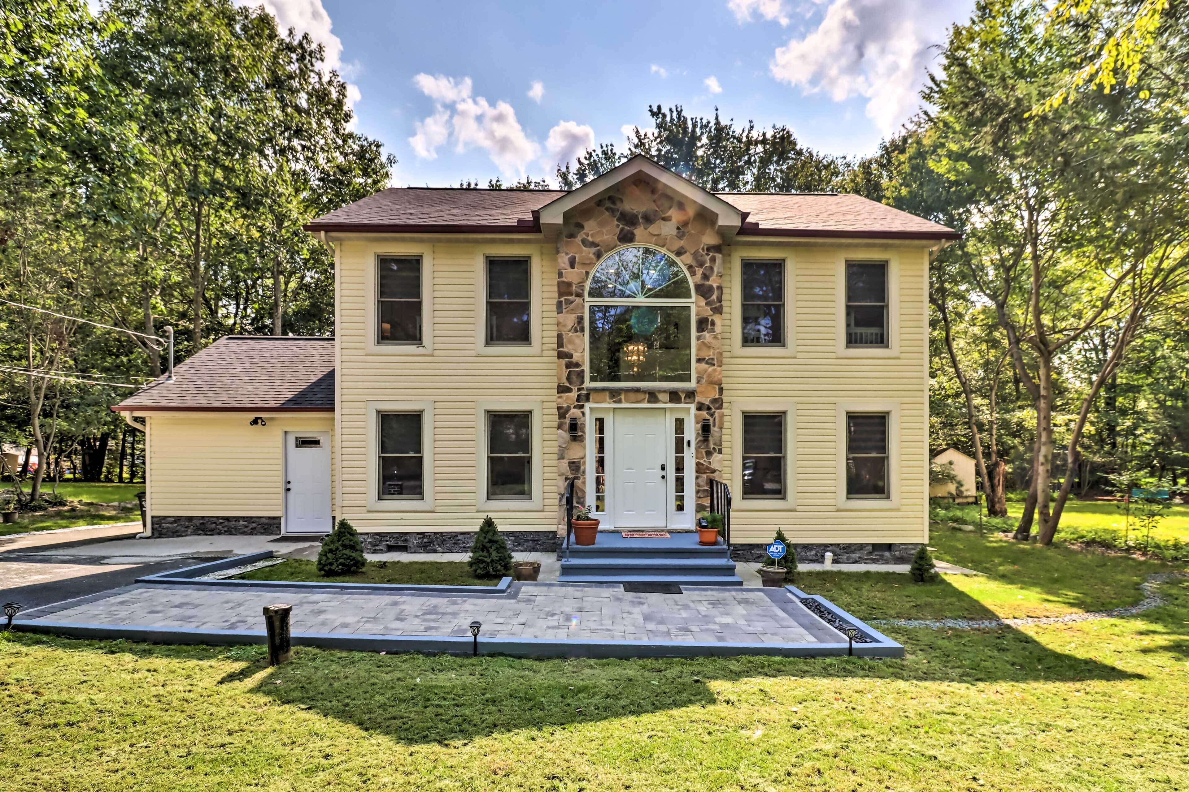 Une maison à deux étages avec une façade en pierre, un porche à l’avant et une allée.