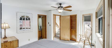 A bedroom with a bed, a ceiling fan, a window, a chair, and a wooden door.