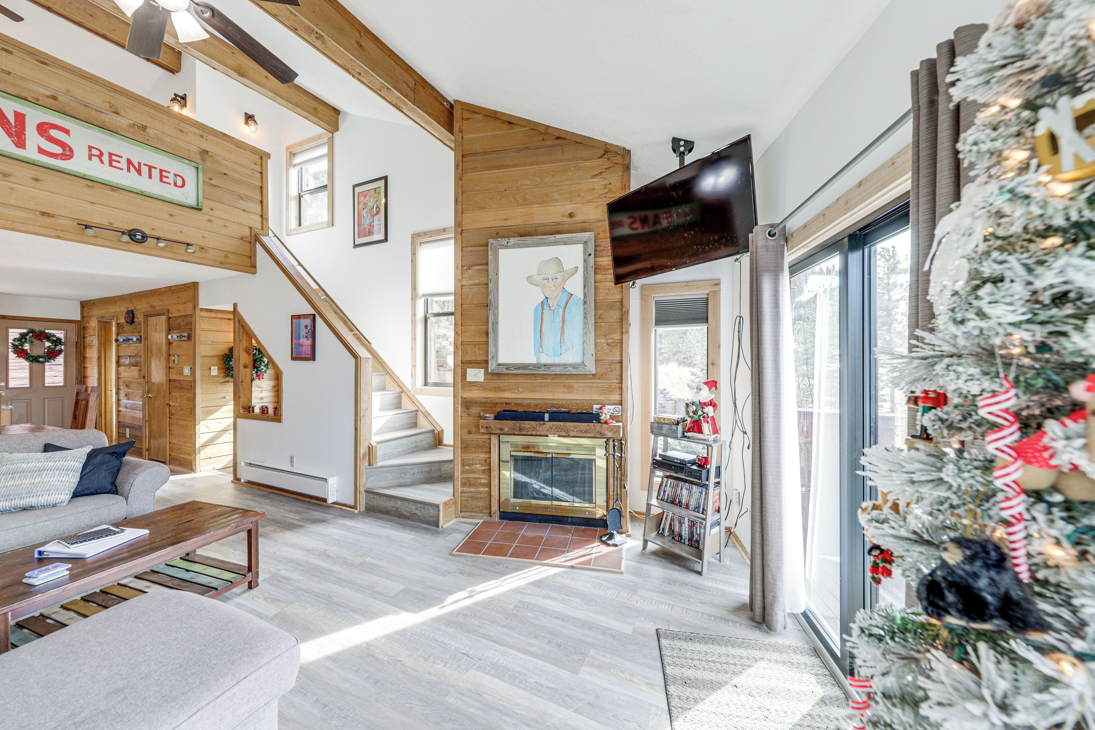 A modern living room with a fireplace, wooden beams, a staircase, and a Christmas tree.