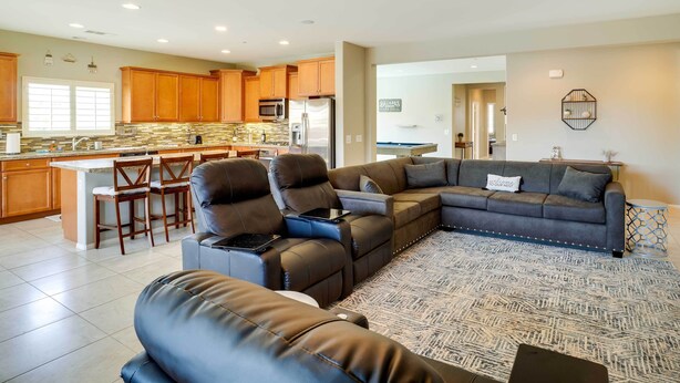 A spacious living area with a large L-shaped sectional sofa, a dining area with wooden cabinets, and a kitchen with a stainless steel refrigerator. - Indio House w/ Pool: 7 Mi to Empire Polo Club! (Indio)