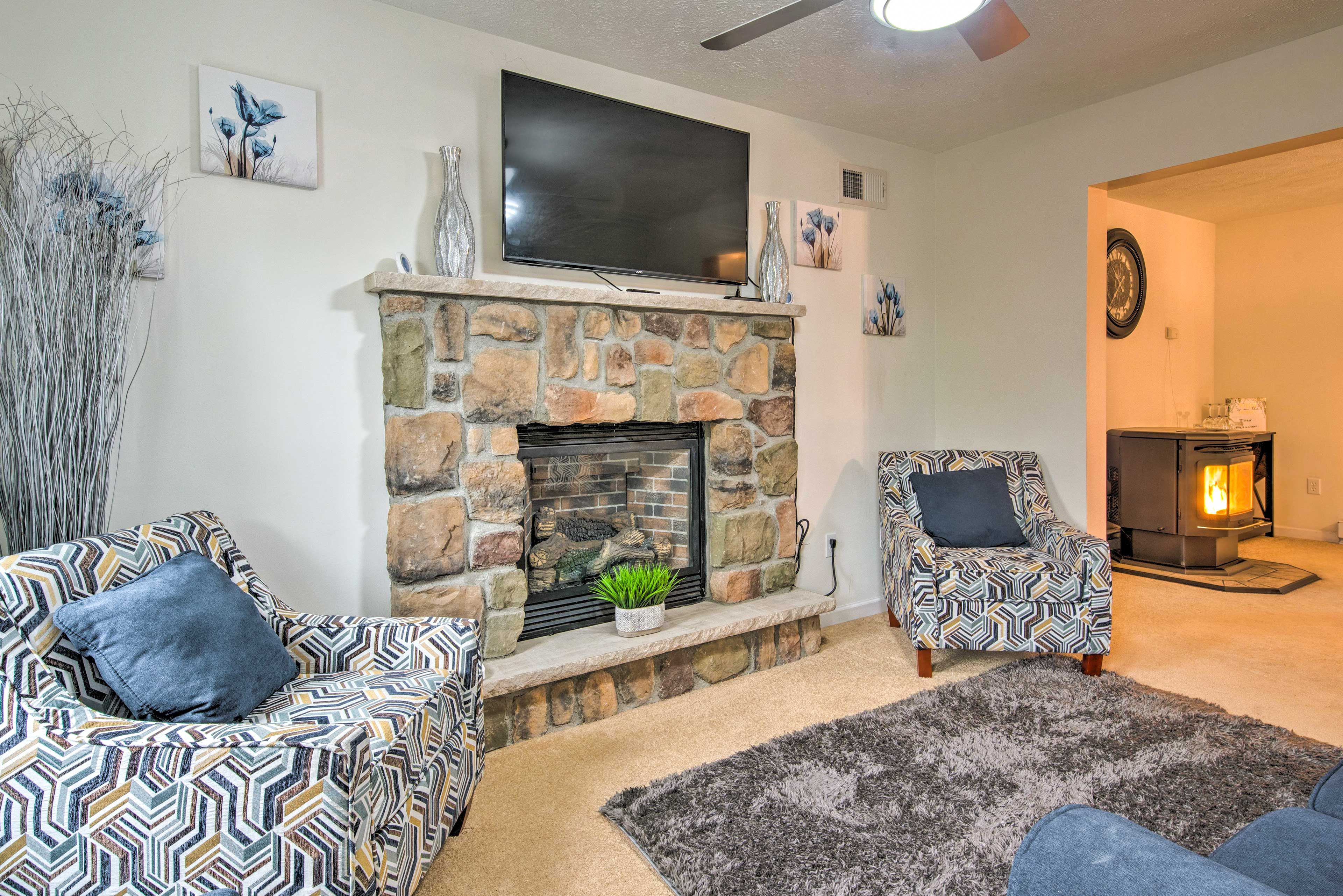 A living room with a stone fireplace, a flat-screen TV mounted above it, patterned sofas, and a rug.