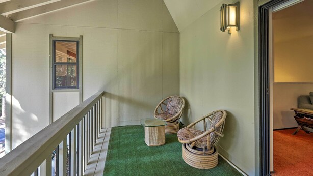 A balcony with a green artificial turf, wicker chairs, a small round table, and a wall-mounted light fixture.