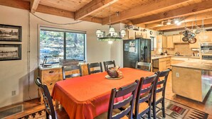 A wooden interior with a dining table, chairs, a chandelier, and a kitchen area.