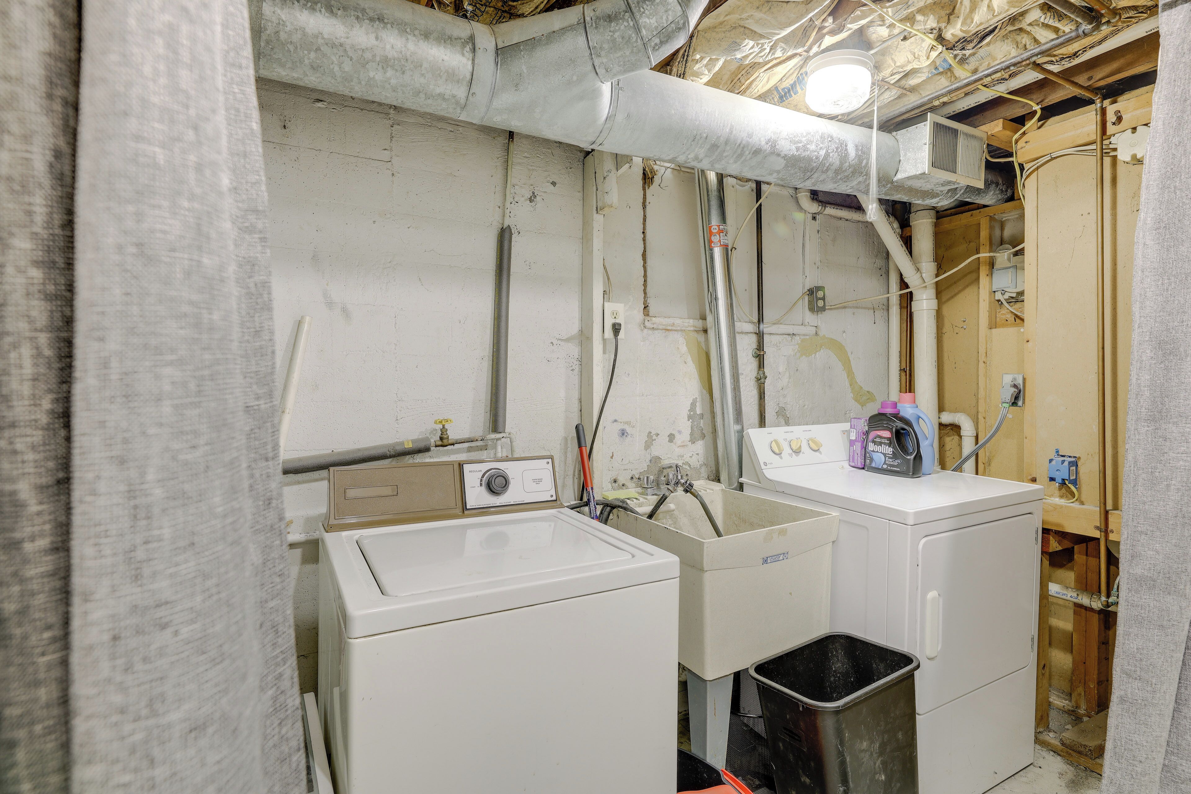 A laundry area with a washing machine, a sink, and a trash bin.