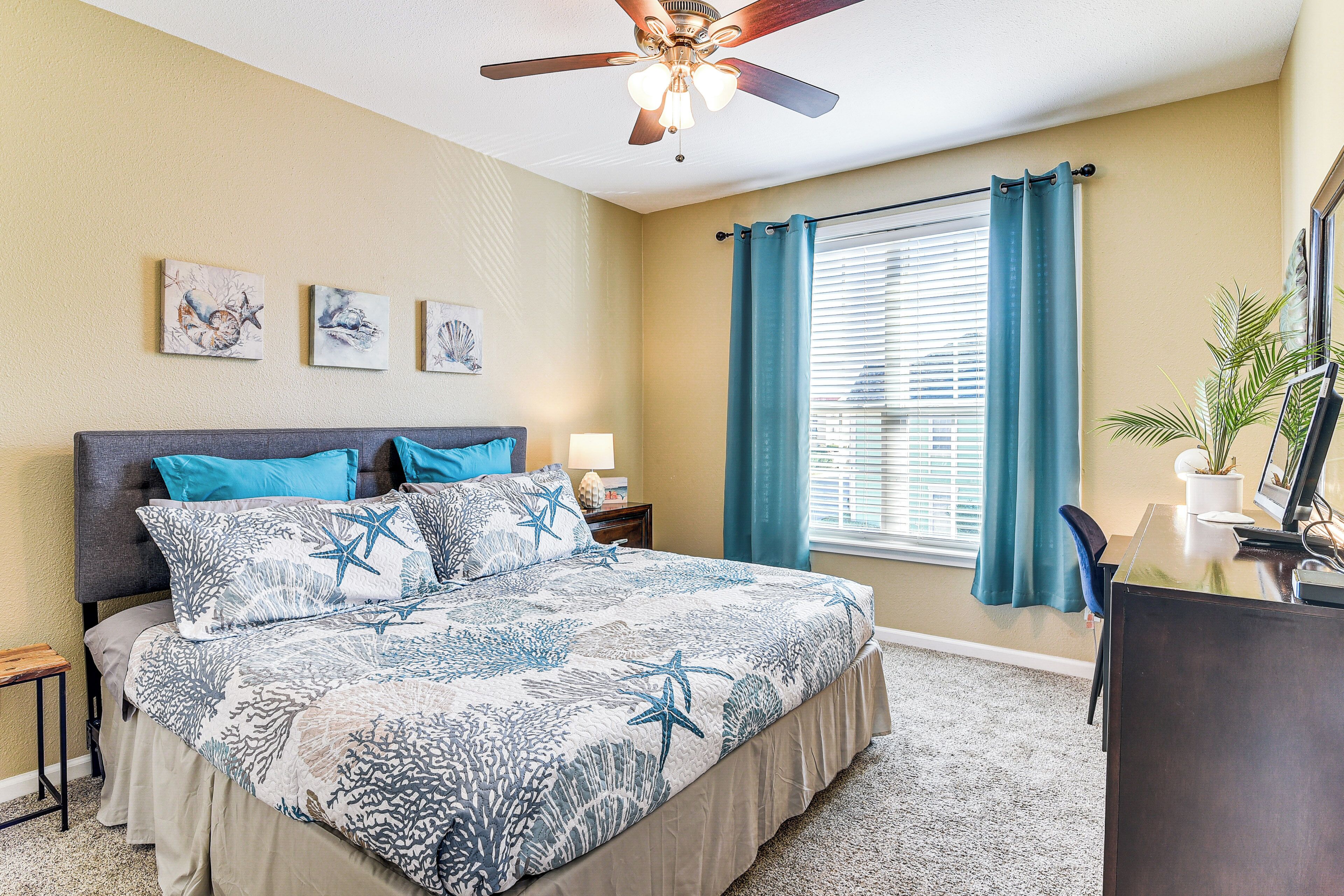 A bedroom with a bed, a ceiling fan, a window with curtains, and wall art.