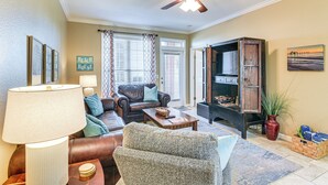 Un salon comprenant un canapé, un fauteuil, une table basse et une lampe. On y trouve également un ventilateur de plafond, une cheminée et une bibliothèque.