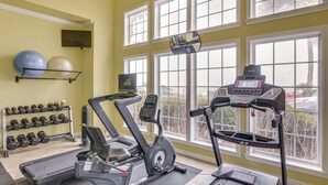 Une salle de sport équipée de tapis de course, d’un vélo elliptique, d’haltères et de ballons d’exercice.