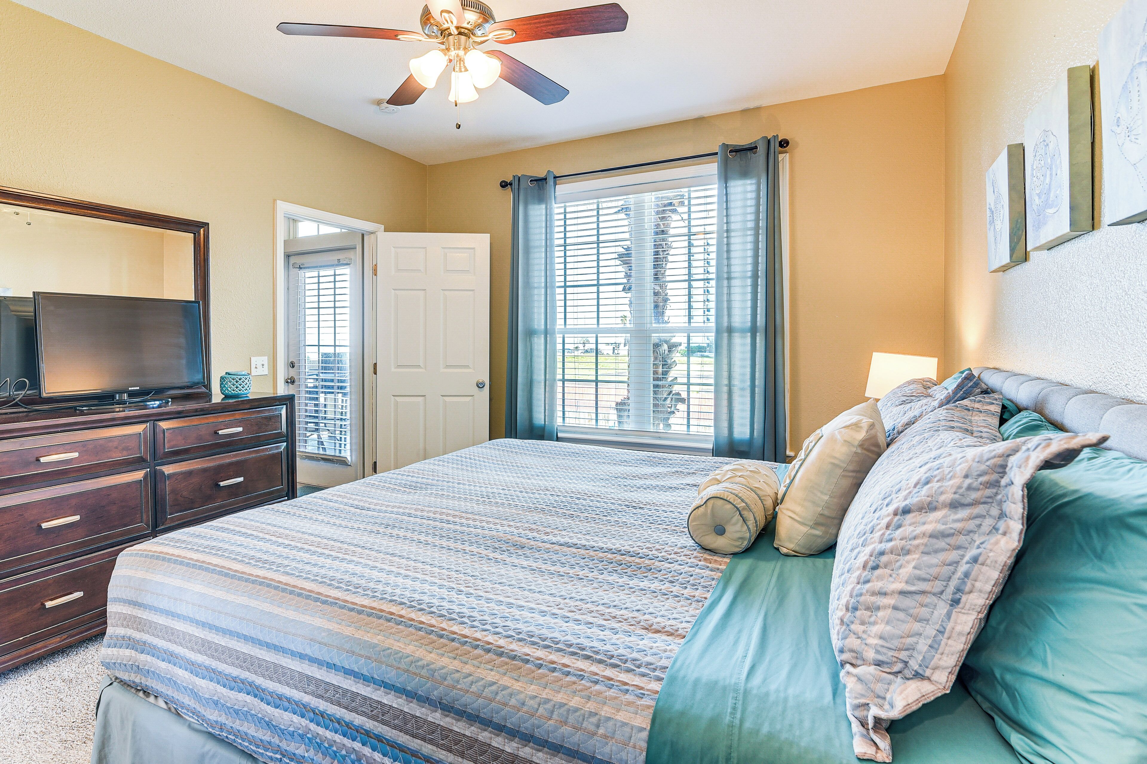 A bedroom with a bed, a dresser, a ceiling fan, and a window with curtains.