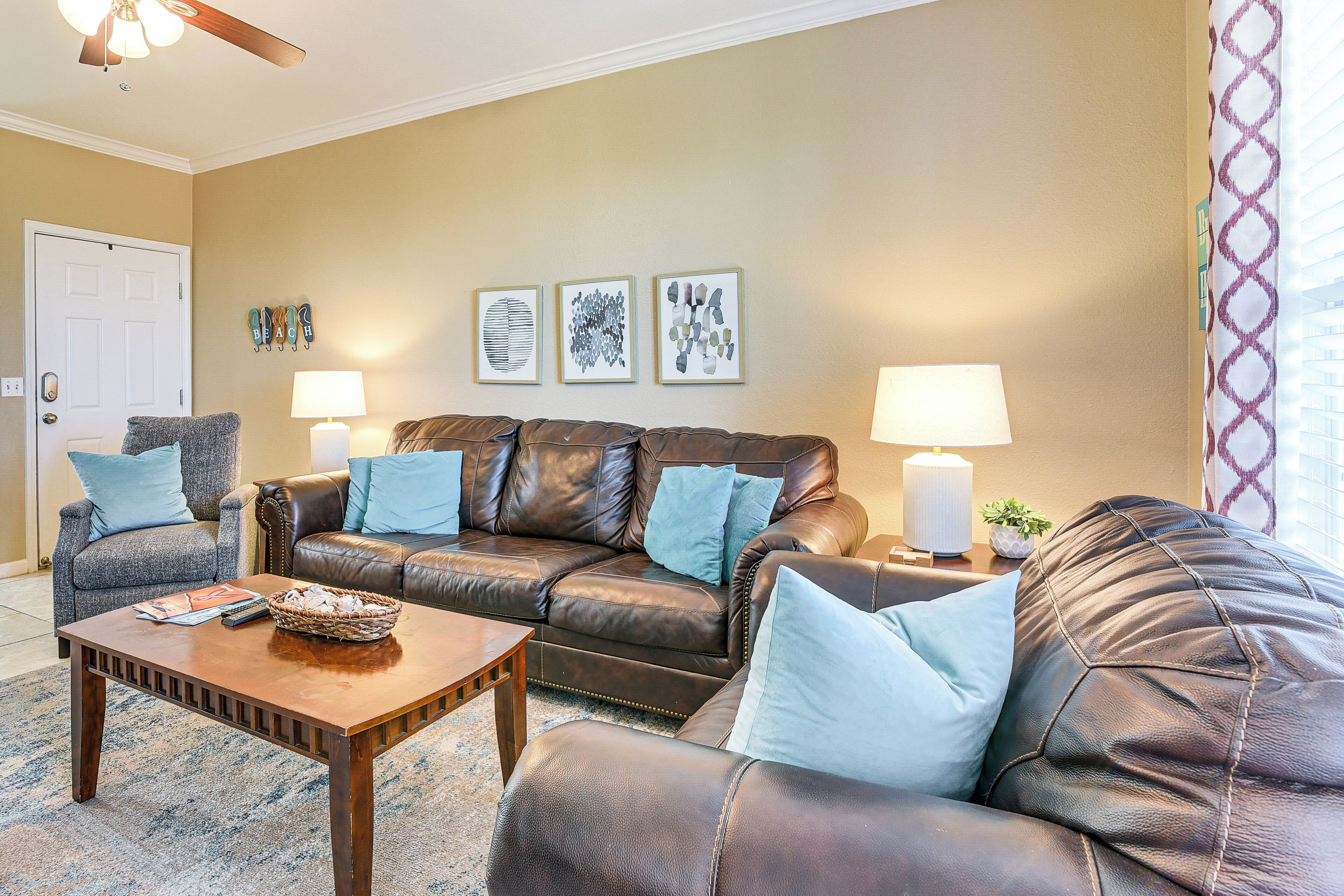 A living room with a brown leather sofa, two side tables with lamps, a coffee table, and wall art.