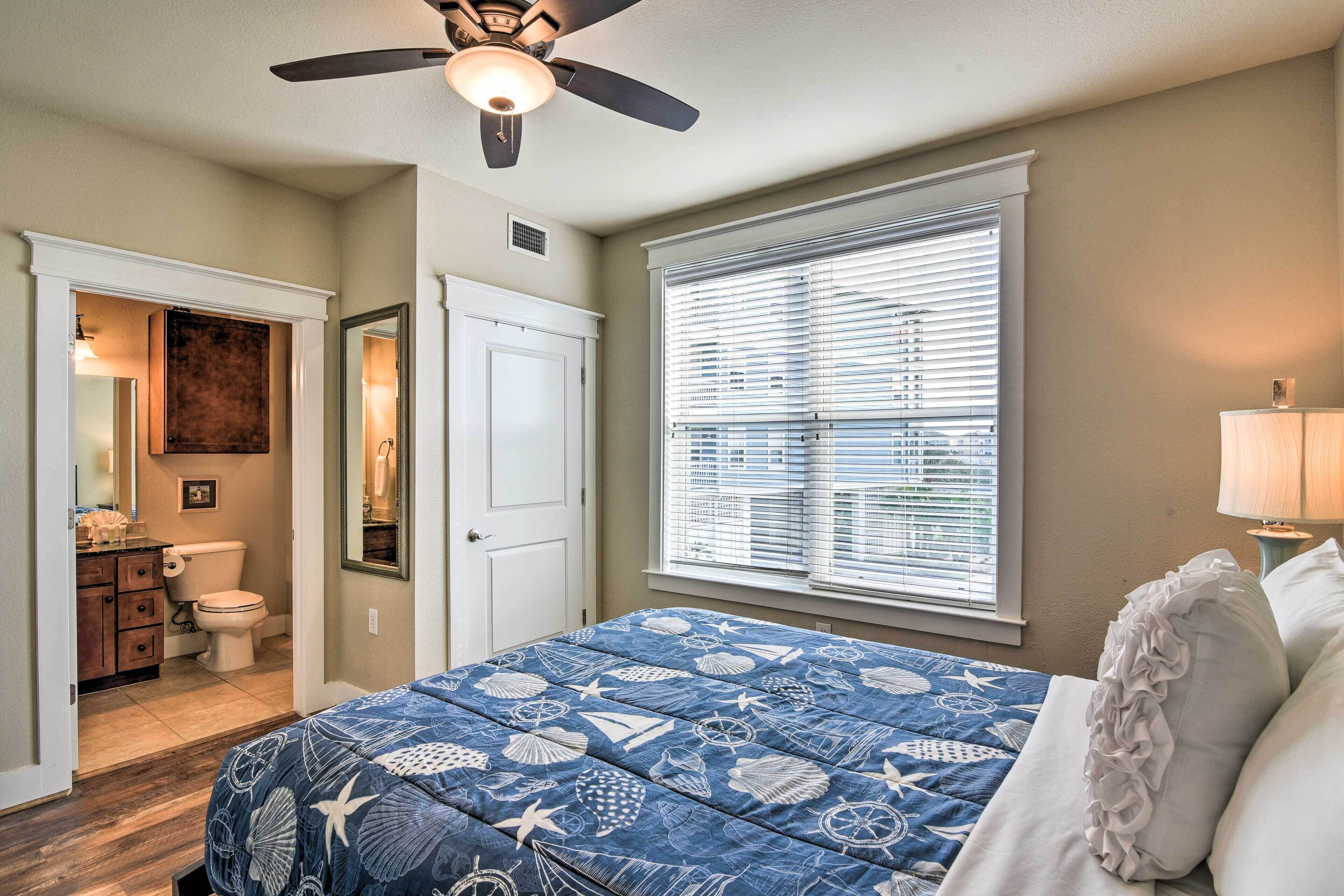 A bedroom with a bed, a ceiling fan, a window with blinds, a nightstand, and a lamp.