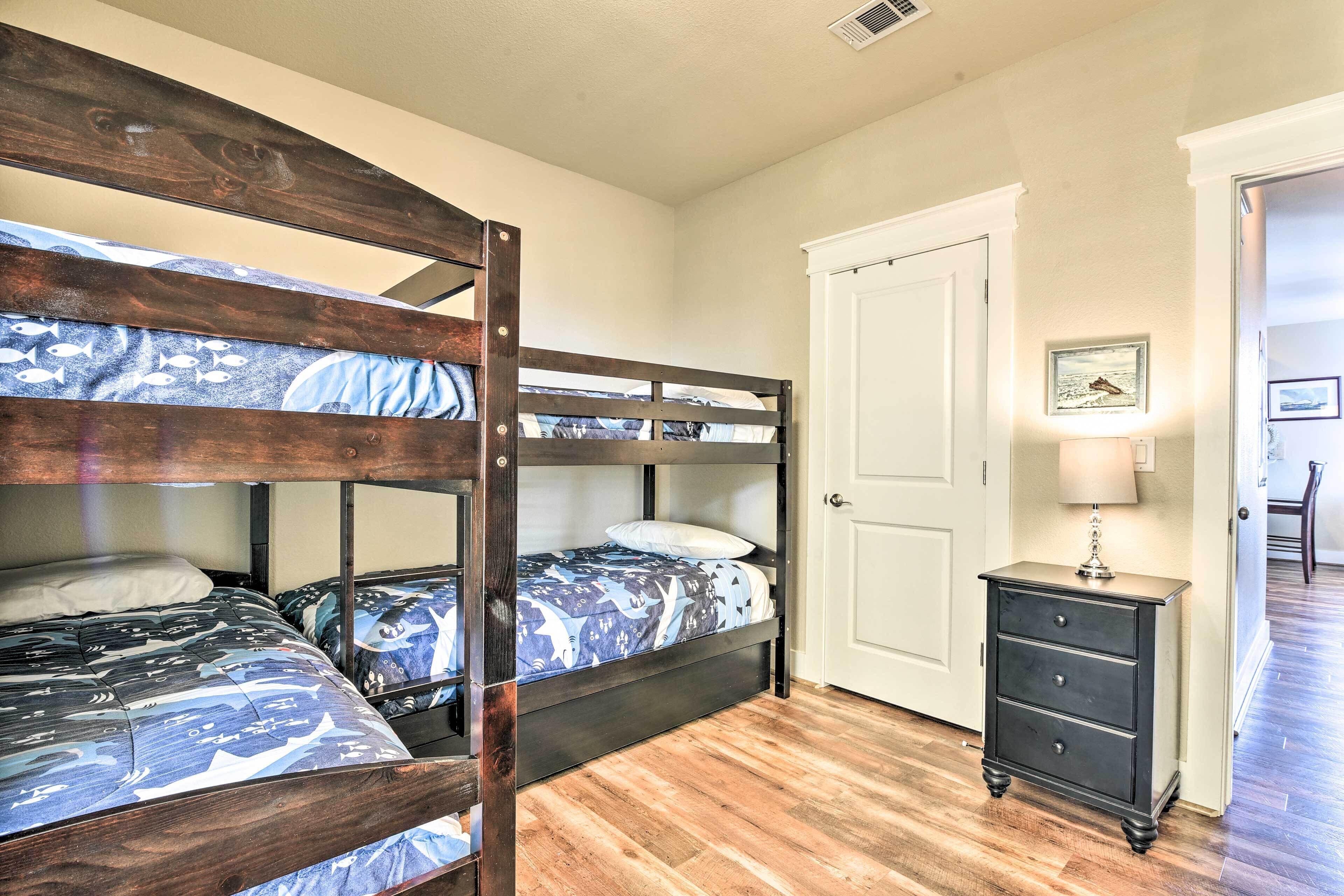 Habitación con literas, cabecera de madera, mesita de noche con cajones y puerta con un marco de fotos.