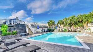 Piscina com espreguiçadeiras, parede de pedra e escadaria que leva a um corrimão branco.